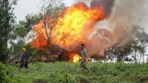 Op deze foto - gemaakt op 10 juni 2012 - loopt een Rakhine boeddhist met zelfgemaakte wapens voor een zojuist in brand gestoken huis van een Rohingya-gezin.